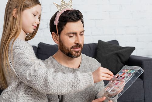 girl holding cosmetic brush near makeup palette in hands of smiling father in crown