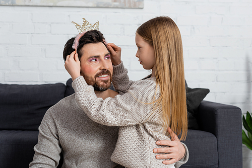 happy girl wearing toy crown on head of father in living room