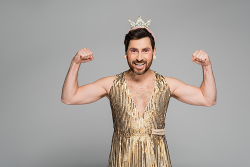 bearded man with toy crown on head and princess dress costume showing muscles isolated on grey