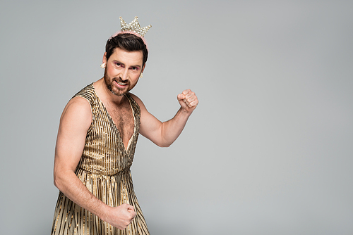 bearded man with toy crown on head and princess dress costume showing muscle isolated on grey