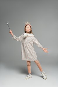full length of happy girl in dress and crown holding toy wand and smiling on grey background