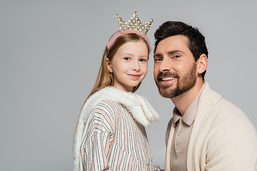 portrait of cheerful father and cute daughter in crown smiling while looking at camera isolated on grey