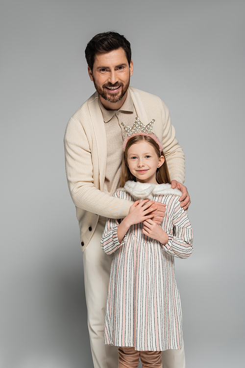 happy bearded man hugging smiling daughter in crown on grey