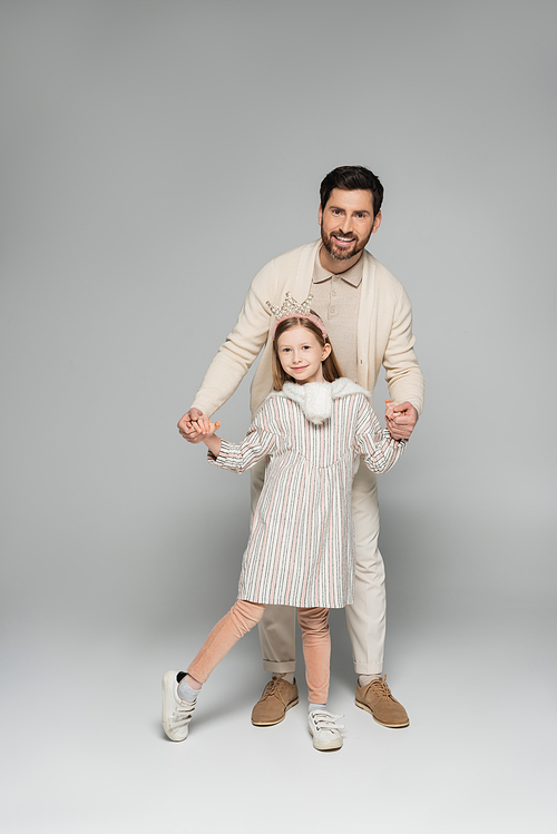 full length of smiling man in white outfit holding hands with happy daughter in grey