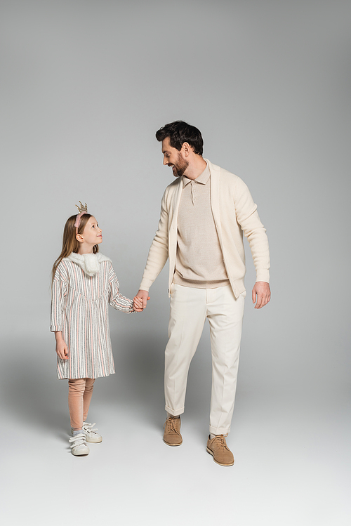 full length of happy father and daughter holding hands while looking at each other on grey