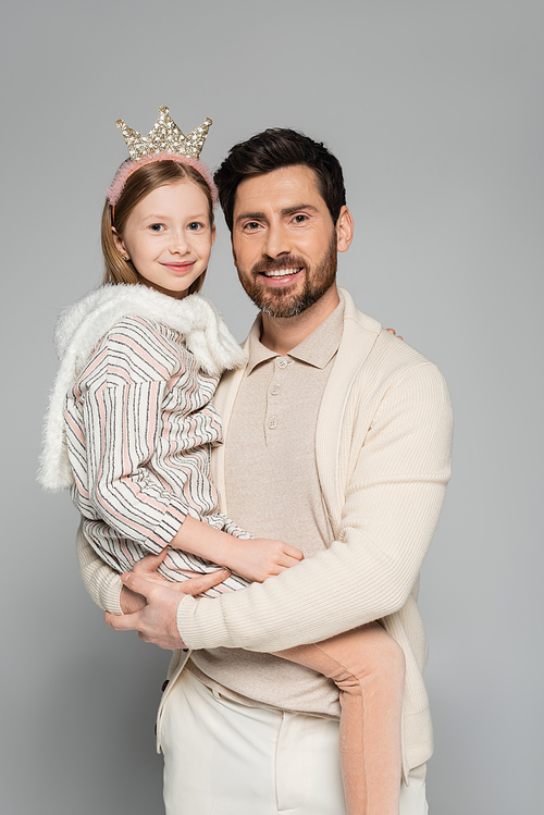 happy father lifting cheerful daughter in crown and dress isolated on grey