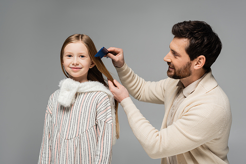 happy bearded father brushing hair of smiling daughter isolated on grey