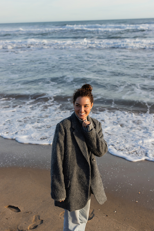 Cheerful woman in coat standing near sea on beach in evening
