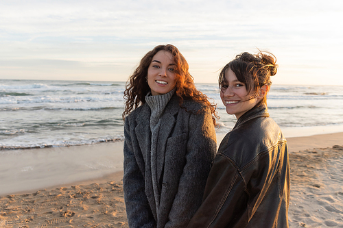 Cheerful young women looking at camera on sandy beach in Spain