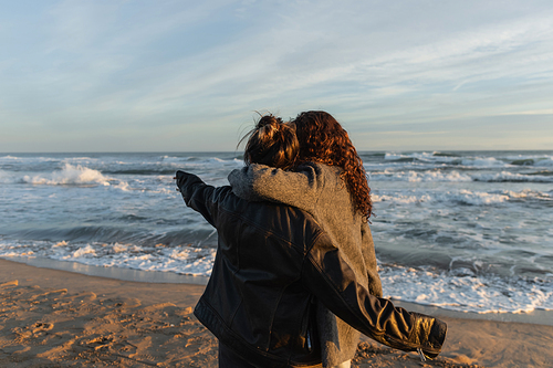 Back view of woman hugging friend on beach in Barcelona