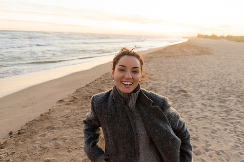 Cheerful young woman looking at camera on beach in evening