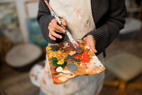 Cropped view of blurred artist in apron holding palette and paintbrush