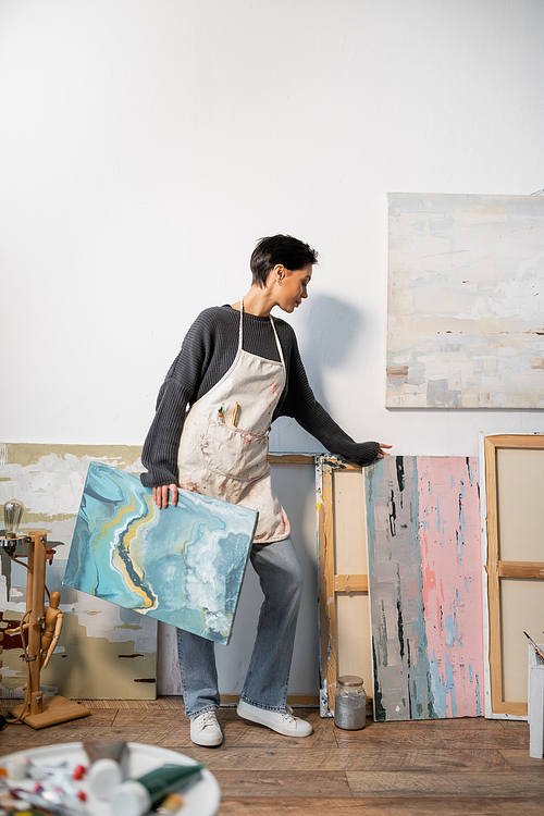 Side view of short haired artist holding paintings in studio
