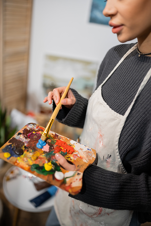 Cropped view of artist in apron mixing paints on palette in workshop