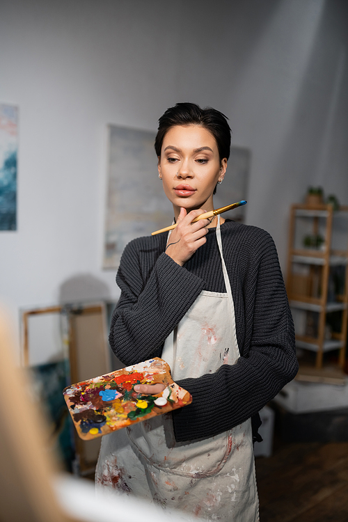 Concentrated artist holding paintbrush and palette in workshop