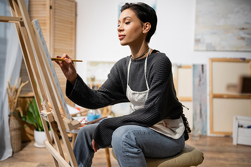 Short haired artist sitting and painting on canvas in studio