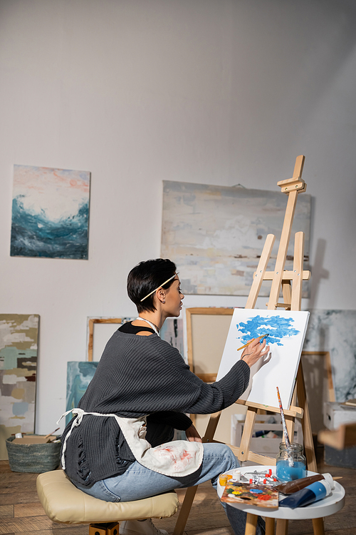 Side view of artist in apron painting on canvas in studio