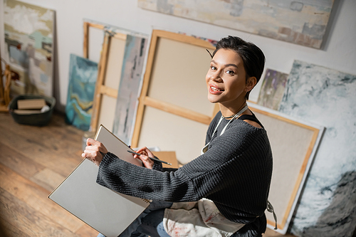 Young short haired artist holding pencil and sketchbook in studio