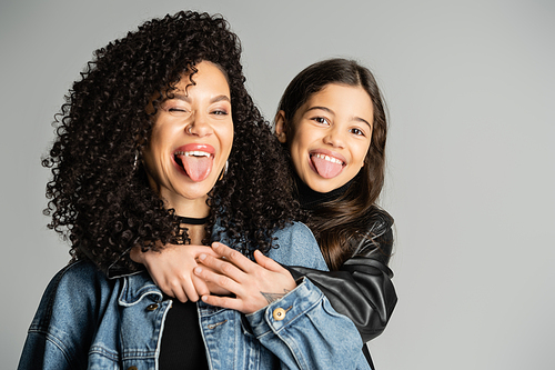Curly woman and daughter sticking out tongues isolated on grey