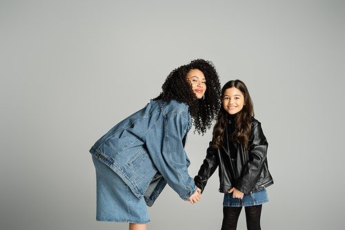 Trendy mother and daughter holding hands isolated on grey