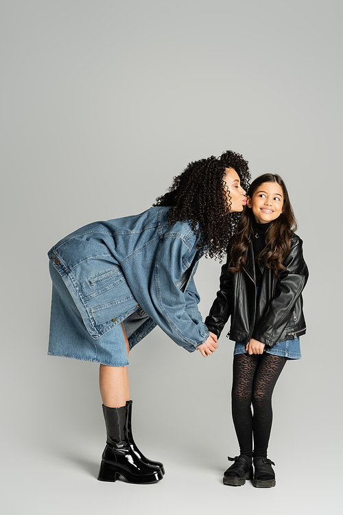 Stylish mother kissing cheerful kid on grey background