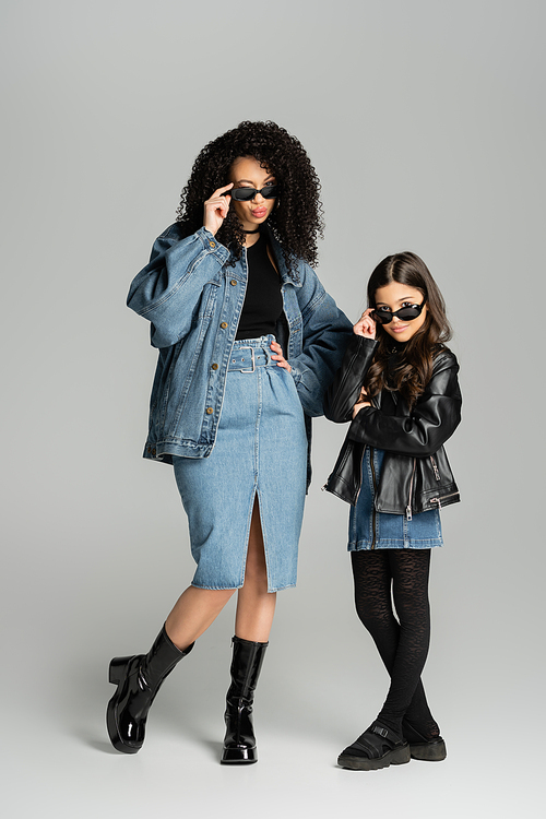 Full length of stylish mother and child posing in sunglasses on grey background