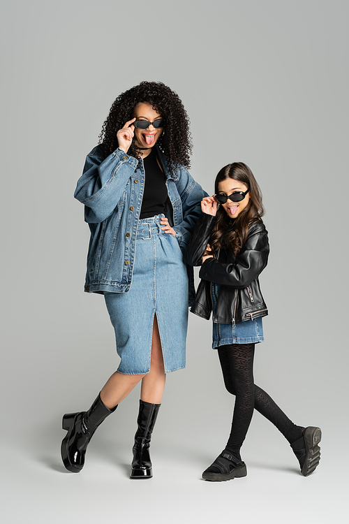 Fashionable mom and daughter in sunglasses sticking out tongues on grey background