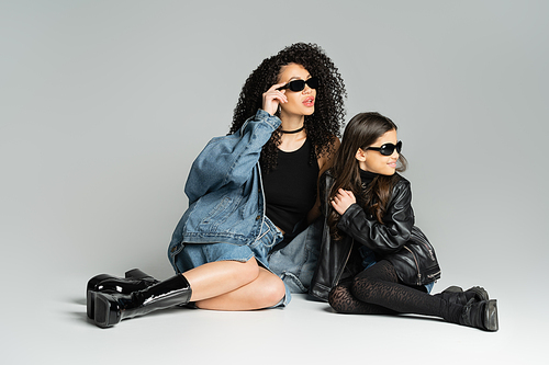 Trendy woman and happy daughter in sunglasses sitting on grey background