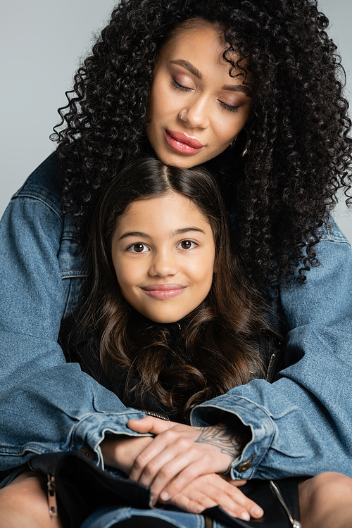 Portrait of curly young mother hugging cheerful child isolated on grey