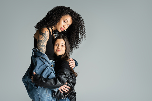 Trendy and tattooed woman hugging child isolated on grey