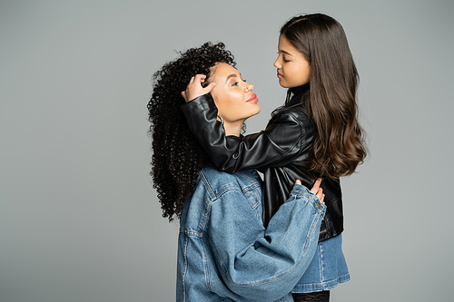 Stylish girl touching hair of mother in denim jacket isolated on grey