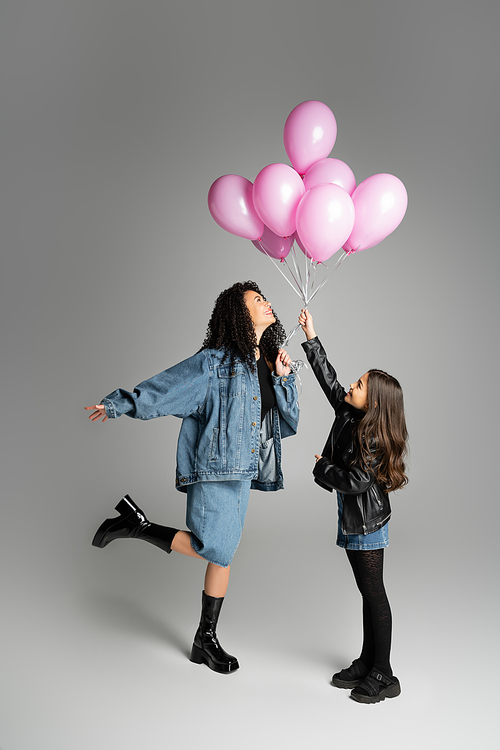 Full length of cheerful mother and kid holding pink balloons on grey background
