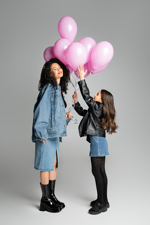 Curly woman and stylish daughter holding balloons on grey background