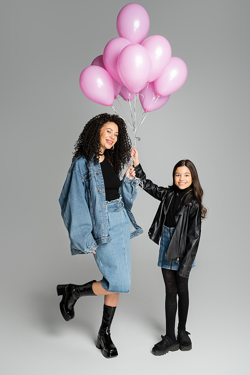Stylish mother and daughter holding pink balloons on grey background