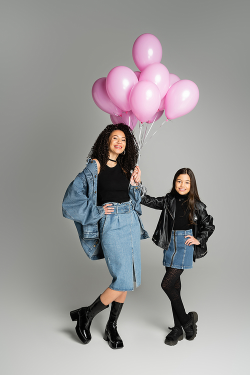 Trendy mother and preteen kid posing and holding balloons on grey background