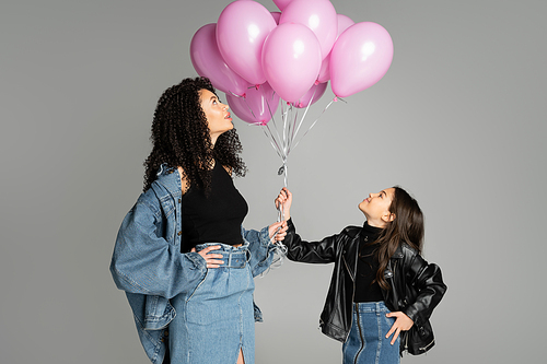 Side view of fashionable mother and child looking at pink balloons isolated on grey