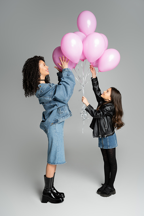 Side view of stylish preteen girl and mom holding pink balloons on grey background