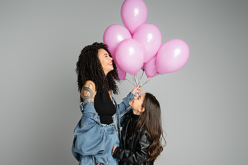 Cheerful mother and preteen daughter holding pink balloons isolated on grey