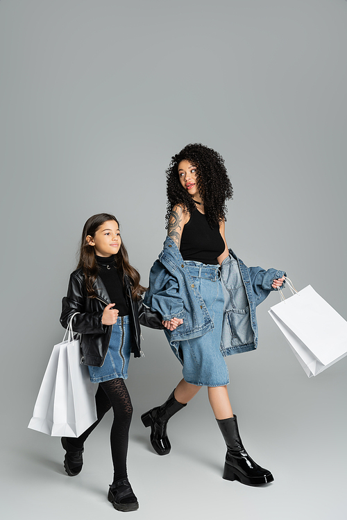 Trendy mom and daughter holding hands and shopping bags on grey background