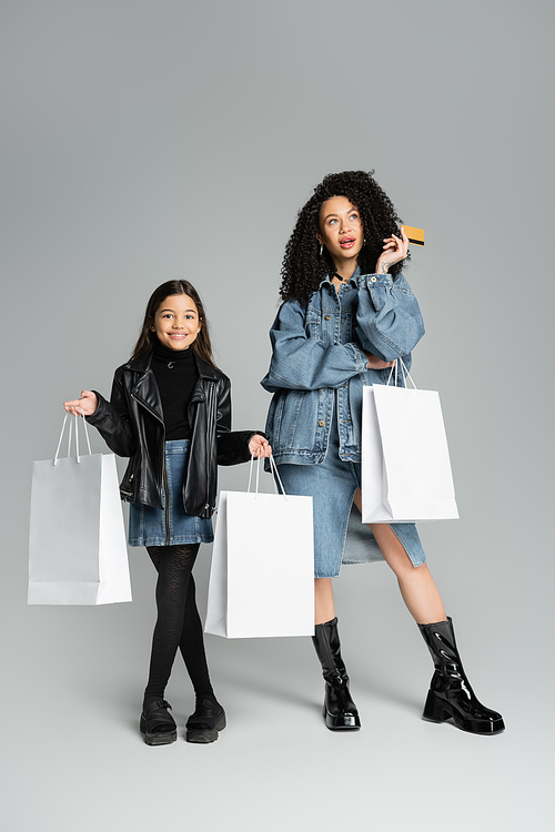 Stylish mother and daughter holding credit card and shopping bags on grey background