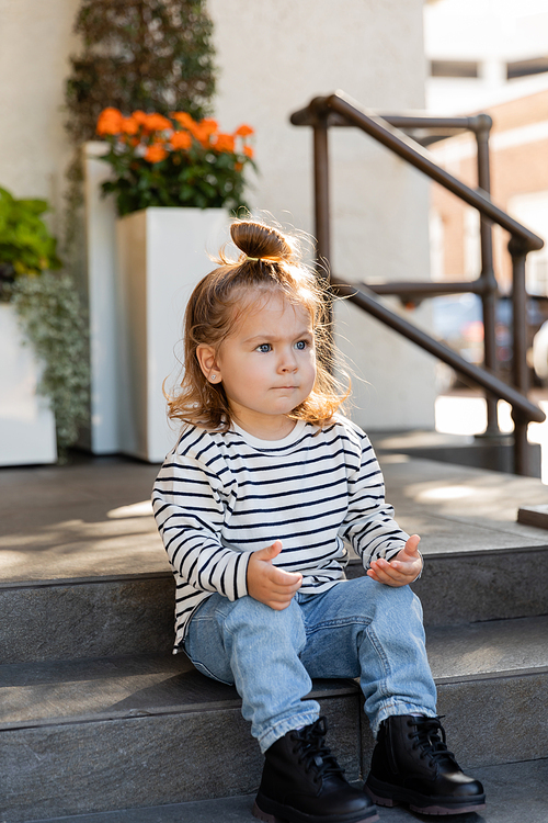 toddler girl in long sleeve shirt and jeans sitting on stairs near house
