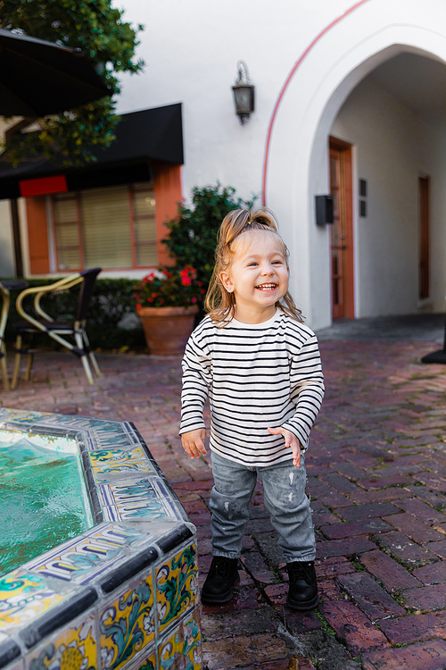 happy toddler girl in striped long sleeve shirt standing near fountain in Miami