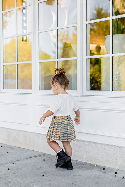 full length of toddler girl in skirt and white t-shirt walking near house