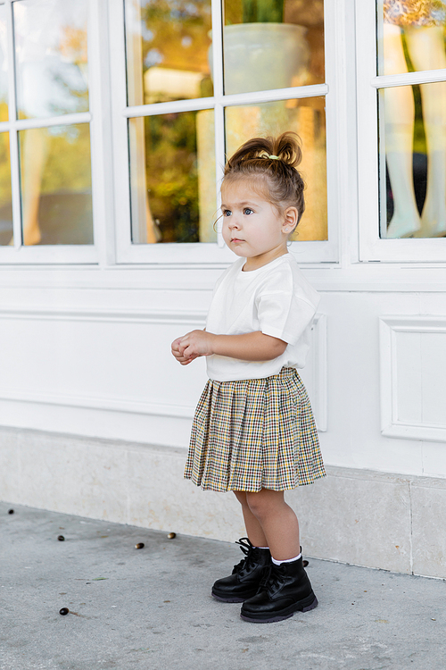full length of toddler girl in skirt and white t-shirt standing near house