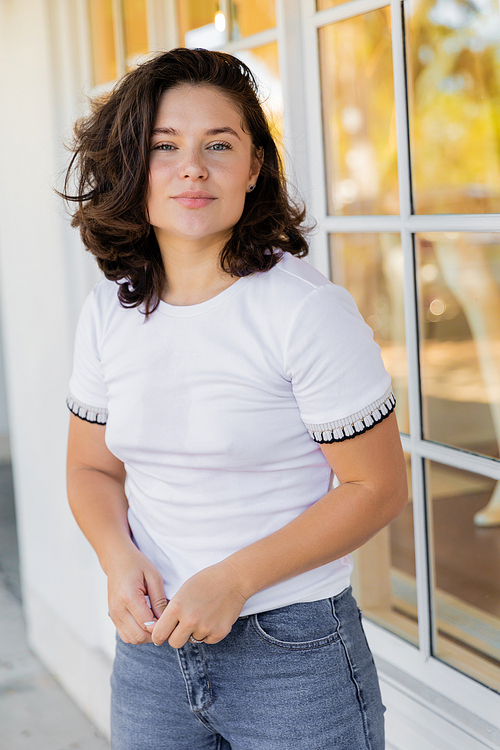portrait of brunette woman in white t-shirt looking at camera near house