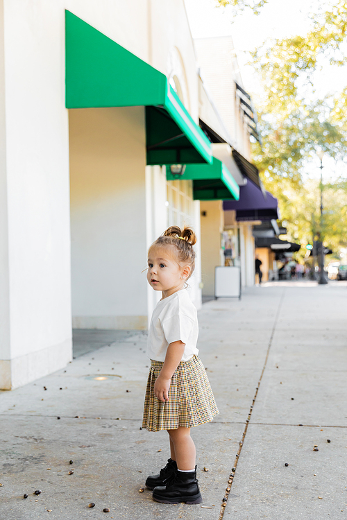 full length of toddler child in skirt and white t-shirt standing near acorns on ground in Miami