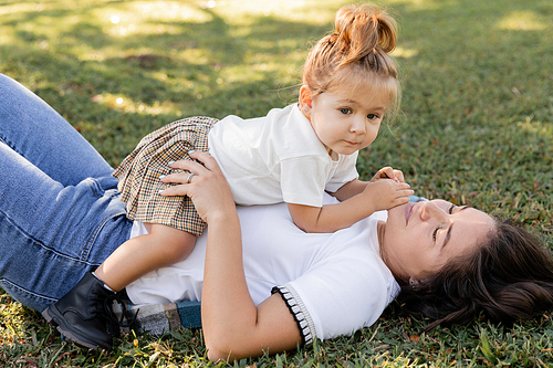 brunette mother lying on green lawn with toddler baby girl