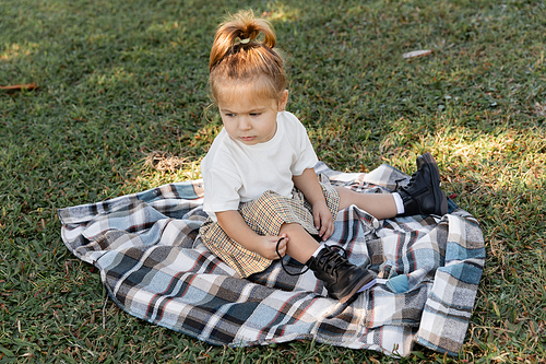 baby girl in checkered skirt and boots sitting on blanket during picnic