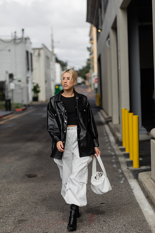 full length of young woman in stylish outfit holding handbag while walking on street in Miami