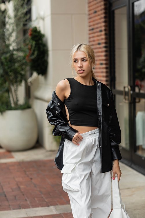 young blonde woman in leather shirt jacket posing with handbag on street in Miami